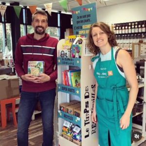 Photo du gérant de la boutique de jouets d'occasion Le Temps des retrouvailles et de la gérante de l'epicerie Day by day à Bourg en Bresse devant un présentoir de jouets d'occasion